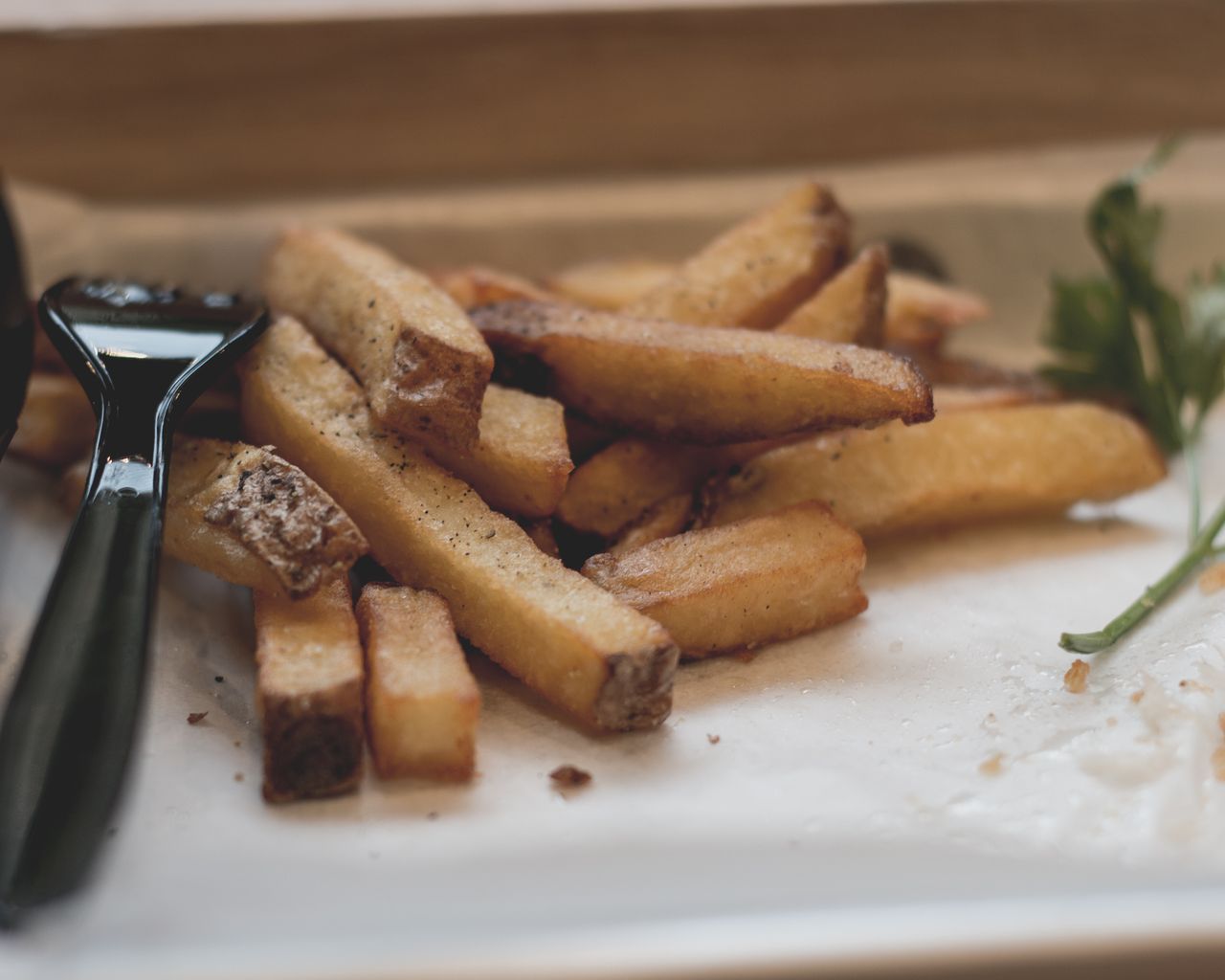 Delicious crispy French fries garnished with herbs on a paper-lined tray. Perfect food photography.
