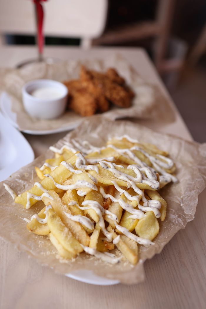 Crispy fries drizzled with mayo served on rustic paper, paired with fried chicken.