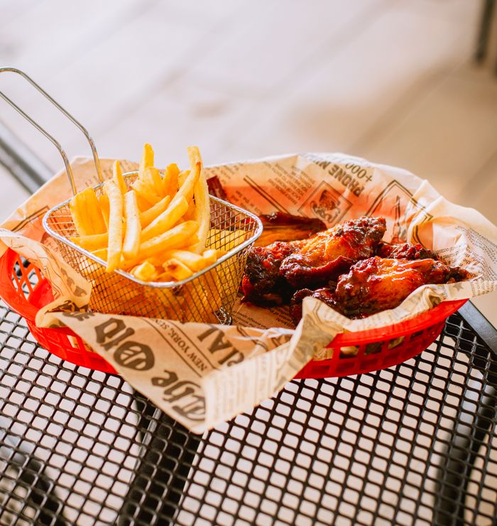 Delicious crispy fries and saucy wings in a basket, perfect for a casual dining experience.